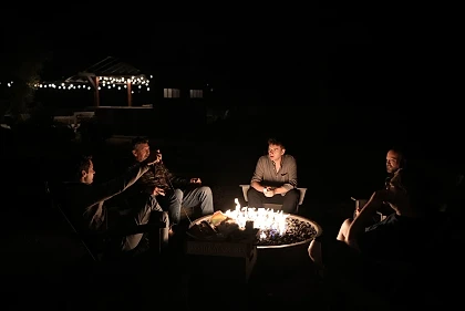 Men sitting in a circle around a lit fire pit at night at a PIVOT Glass House retreat